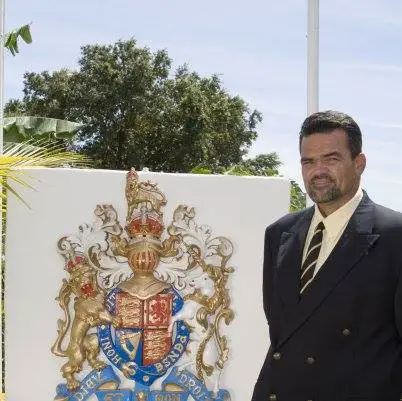 Photo of M J Harper in a suit in front of a British crest, representing the United Kingdom consulate in the Bay Islands