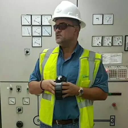 M J Harper with a hardhat and reflective vest, standing in front of electrical equipment at RECO (Roatan Electric Company)
