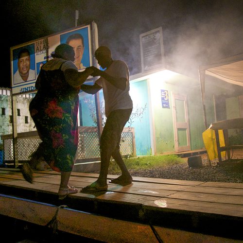 A St. Helene couple dance political candidates for the National Party look on from their campaign posters ( photo credit Tom Leopold )